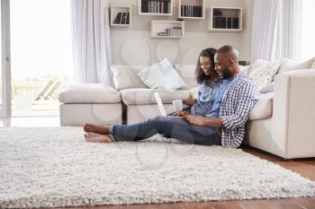 Young black couple sit on the floor using laptop, side view