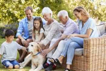Three generation family petting a dog in the garden