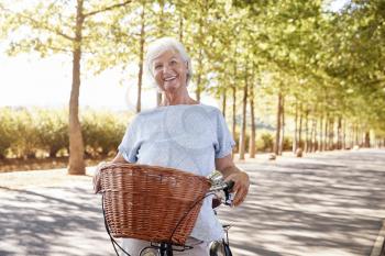 Portrait Of Smiling Senior Woman Cycling On Country Road
