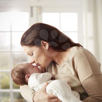 Loving Mother Kissing And Cuddling Newborn Baby At Home