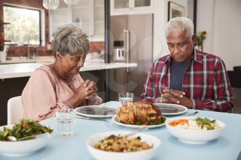 Senior Couple Saying Grace Before Meal Around Table At Home