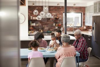Multi Generation Family Praying Before Meal Around Table At Home