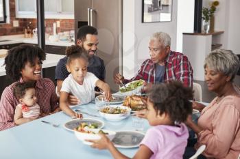 Multi Generation Family Enjoying Meal Around Table At Home