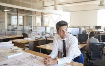 Young male architect leaning on desk in open plan office
