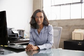 Young mixed race woman at office desk looking to camera