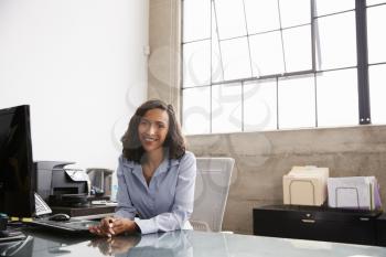 Young mixed race woman at office desk smiling to camera
