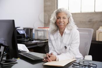 Senior female doctor sitting at desk in an office, portrait