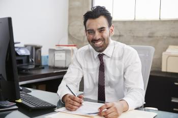 Young Hispanic male professional at desk smiling to camera
