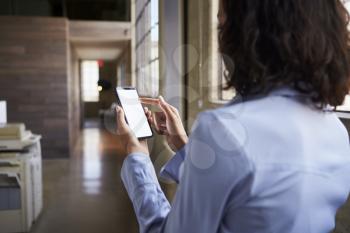 Young businesswoman using smartphone in office, back view