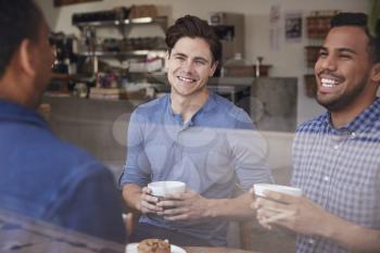 Three male friends laughing over coffee at a coffee shop