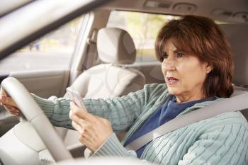 Senior woman in car using her smartphone while driving