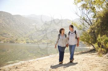 Senior couple hold hands hiking by a mountain lake