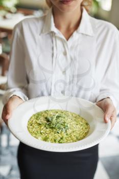 Close Up Of Waitress Holding Plate Of Pea And Mint Risotto In Restaurant
