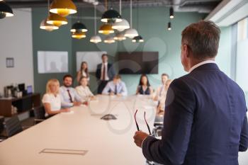 Mature Businessman Addressing Group Meeting Around Table At Graduate Recruitment Assessment Day