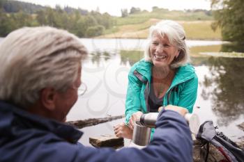 Senior couple by a lake, man pouring coffee to his wifes cup, over shoulder view, Lake District, UK