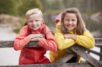 Two children leaning on a wooden fence in the countryside smiling to camera, close up