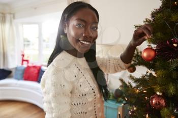 Portrait Of Woman Hanging Decorations On Christmas Tree At Home