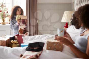 Young mixed race girl carrying gifts in her parents bedroom on Christmas morning, parents sitting up in bed, close up