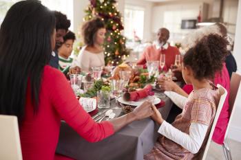 Multi generation, mixed race family holding hands and saying grace at the Christmas dinner table, side view