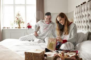 Excited Couple In Bed At Home Opening Gifts On Christmas Day
