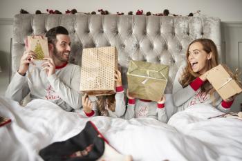 Excited Family In Bed At Home Shaking Gift Boxes On Christmas Day