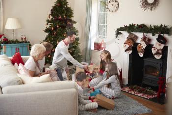 Three Generation Family Wearing Pajamas In Lounge At Home Opening Gifts On Christmas Day