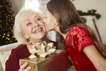 Grandmother Receiving Christmas Gift From Granddaughter At Home