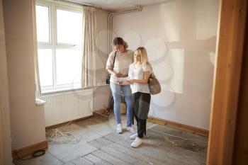 Two Female Friends Buying House For First Time Looking At House Survey In Room To Be Renovated
