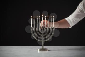 Hand Placing Lit Candle On Metal Hanukkah Menorah On Marble Surface Against Black Studio Background