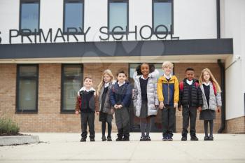 Primary school kids standing in front of their school looking to camera, full length, low angle