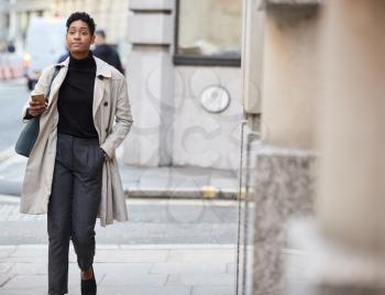 Young black businesswoman walking in the street in London holding smartphone, selective focus