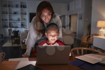 Hispanic woman looking over her sons shoulder while he does his homework using laptop computer
