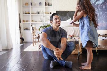 Hispanic dad sitting on the floor in sitting room listening his young daughter, side view