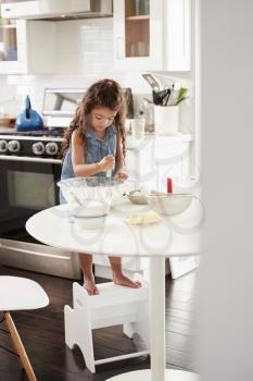 Young girl making a cake in the kitchen on her own, mixing cake mix with a whisk, vertical