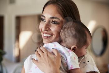 Smiling millennial mother holding her newborn son close to her chest, head and shoulders, close up