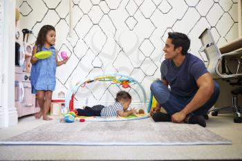 Young girl playing tea party with dad, sitting on the floor, baby brother on a play mat beside them