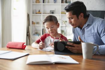 Hispanic pre-teen boy sitting at dining table working with his home school tutor