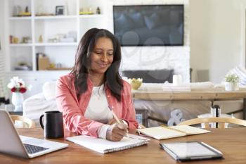 Smiling mixed race retired woman sitting at a table writing in her dining room, waist up