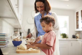Millennial woman and her toddler son preparing food together standing at a worktop in the kitchen, side view, close up, selective focus