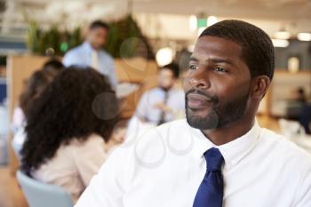 Businessman In Modern Office With Colleagues Meeting Around Table In Background