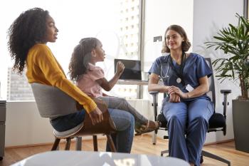 Mother And Daughter Having Consultation With Female Pediatrician Wearing Scrubs In Hospital Office