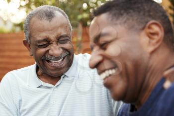 Senior black man and his adult son laughing together outdoors, close up