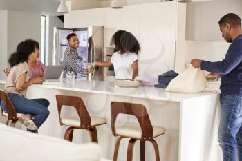 Black family in their kitchen, unpacking groceries and putting them away together