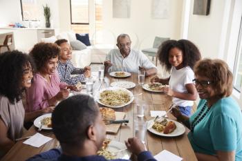 Three generation black family sitting at the table talking and eating dinner together, close up