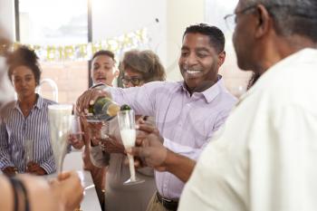 Middle aged black man pouring champagne to celebrate with his three generation family, close up