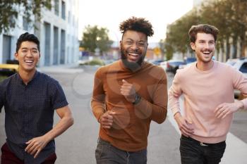 Three hip young adult male friends running for fun in a city road, front view, close up