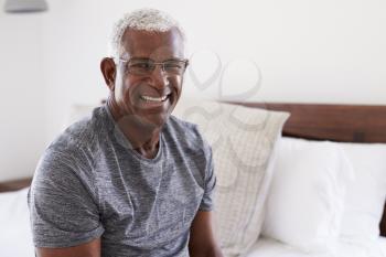Portrait Of Smiling Senior Man Sitting On Side Of Bed At Home Looking Positive