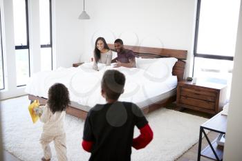 Children Running Into Parents Bedroom With Gift And Card In Bed To Celebrate Mothers Day Or Birthday