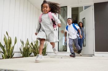 Excited Children Running Out Of Front Door On Way To School Watched By Mother