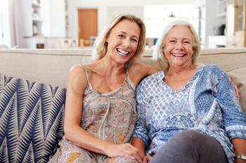 Portrait Of Smiling Mother With Adult Daughter Relaxing On Sofa At Home